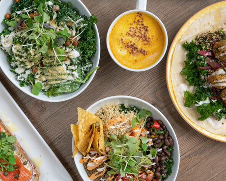 Overhead view of healthy meals with kale salads, a grain bowl with beans and a wrap on a wooden table